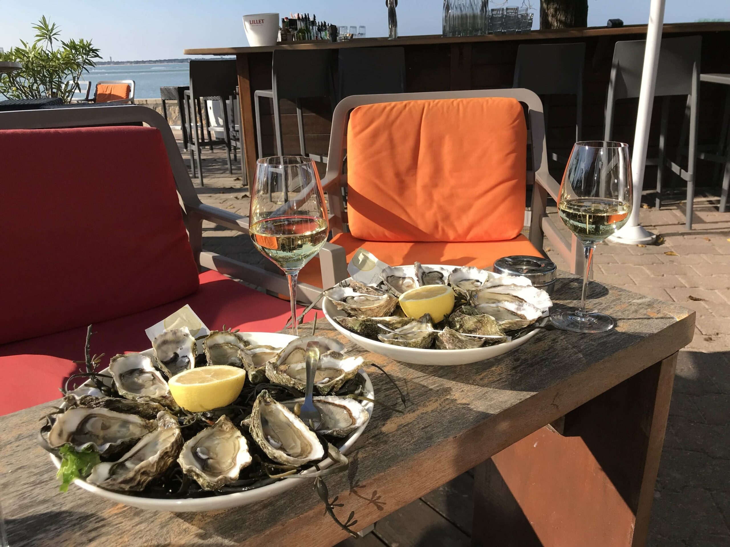 Table pour deux personnes près de la mer, avec deux verres de vins, et deux plateaux d'huitres