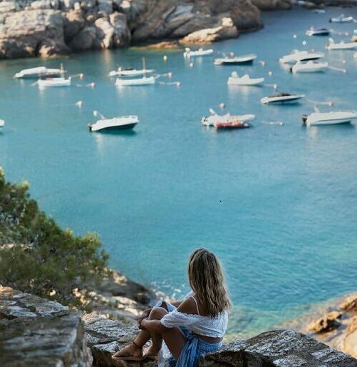 Femme assise sur des rochers observant des bateaux au loin sur la mer